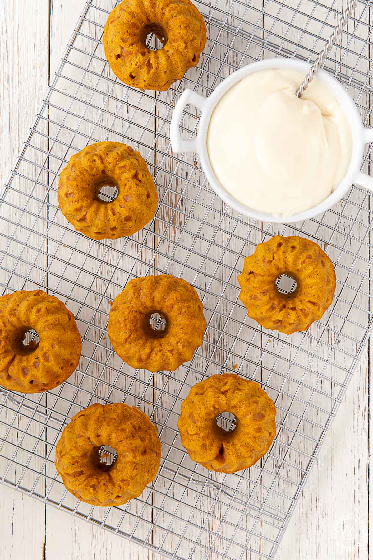 mini pumpkin spice bundt cakes on a cooling rack with a bowl of frosting