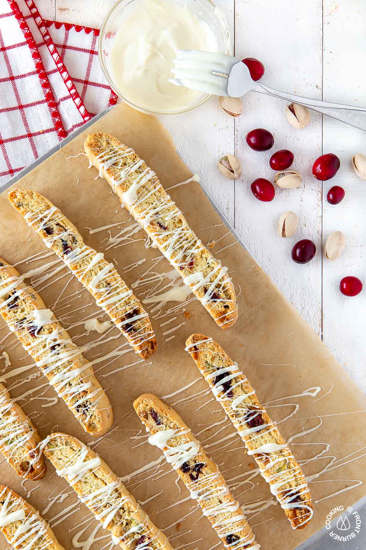 cranberry pistachio biscotti drizzled with white chocolate on a cookie sheet