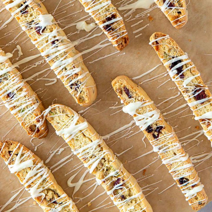 cranberry pistachio biscotti on parchment paper drizzled with white chocolate