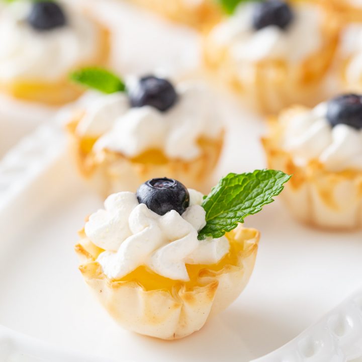 a phyllo cup with lemon curd topped with whipped cream and sprig mint