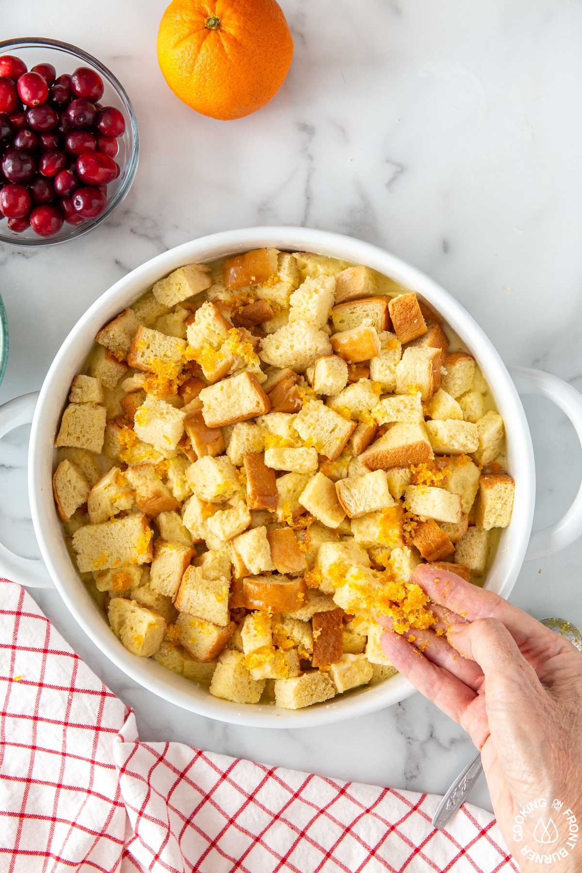 sprinkling orange sugar mixture on cubed bread in a baking dish