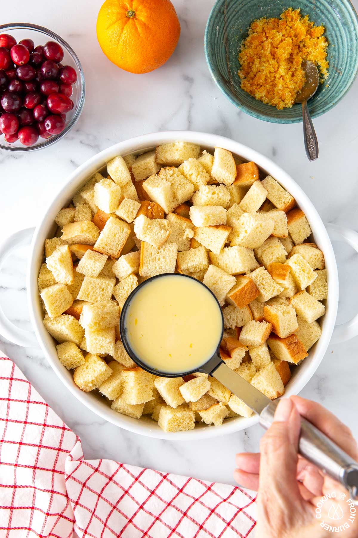 white baking dish with cubed bread; pouring over an egg mixture