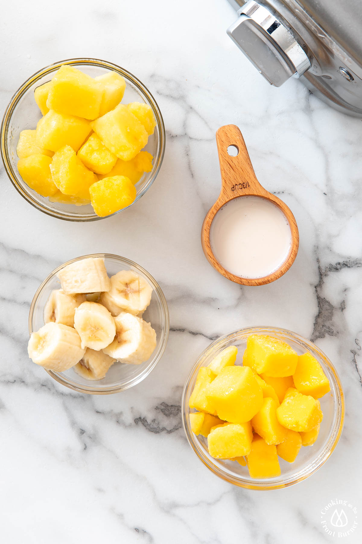 frozen mango, banana and mango in bowls; cup of almond milk