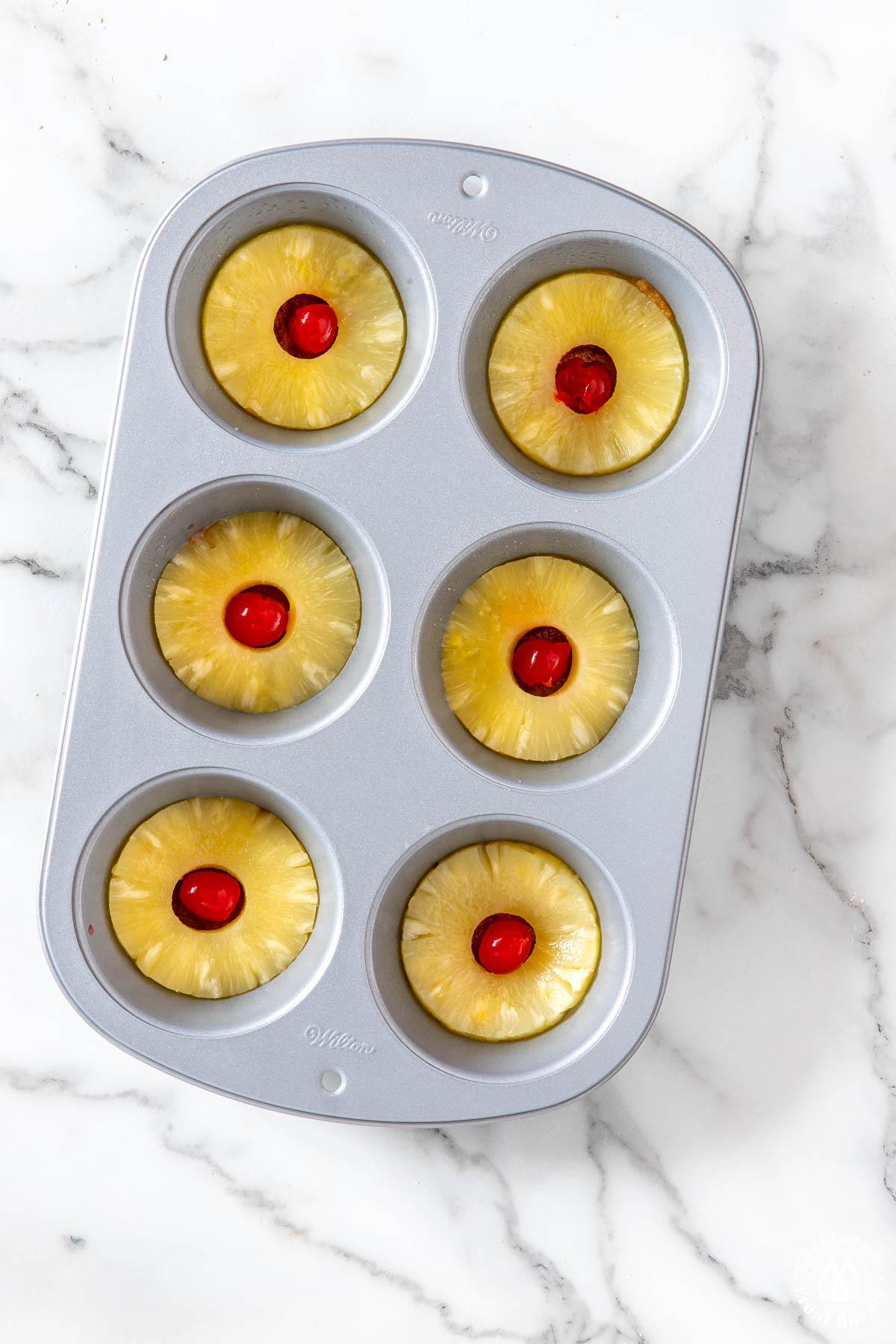 muffin tin with pineapple slice and a cherry in middle