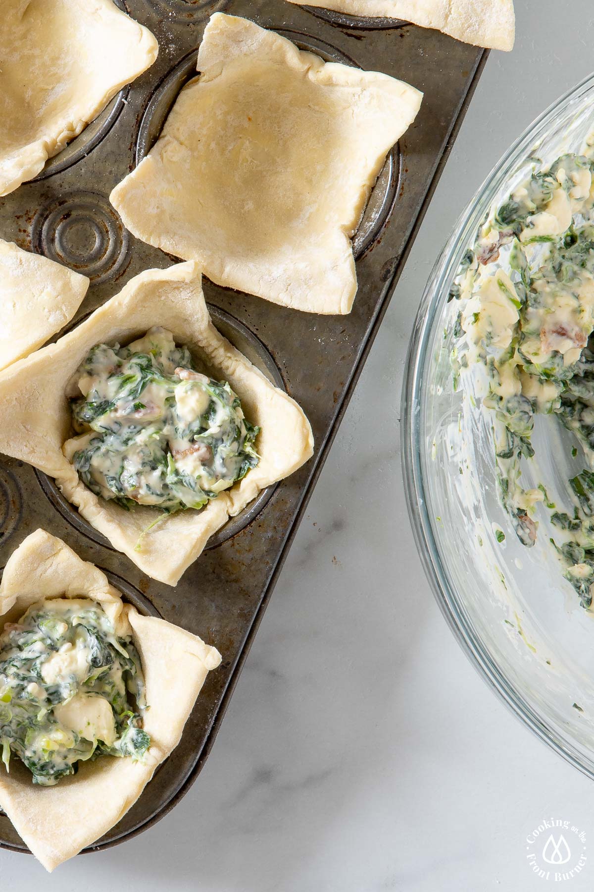 muff tin with puff pastry squares pressed in and spinach filling in each