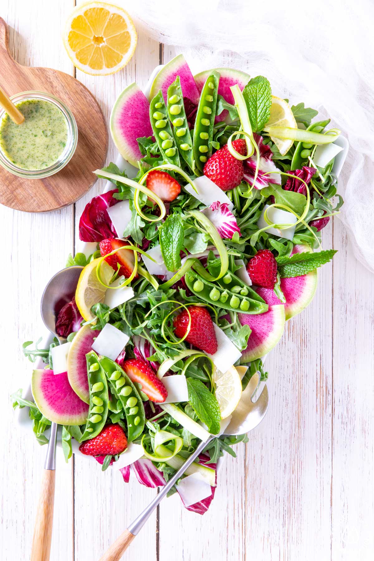 spring salad on a white plate with serving tongs