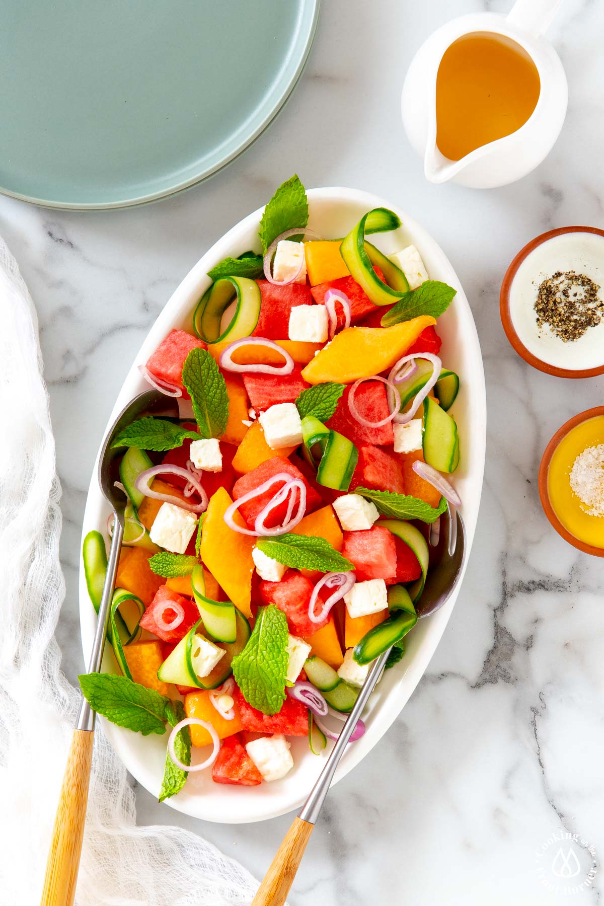 white oval platter with melon salad and serving tongs