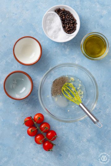 small clear bowl with garlic, pepper salt and a whisk