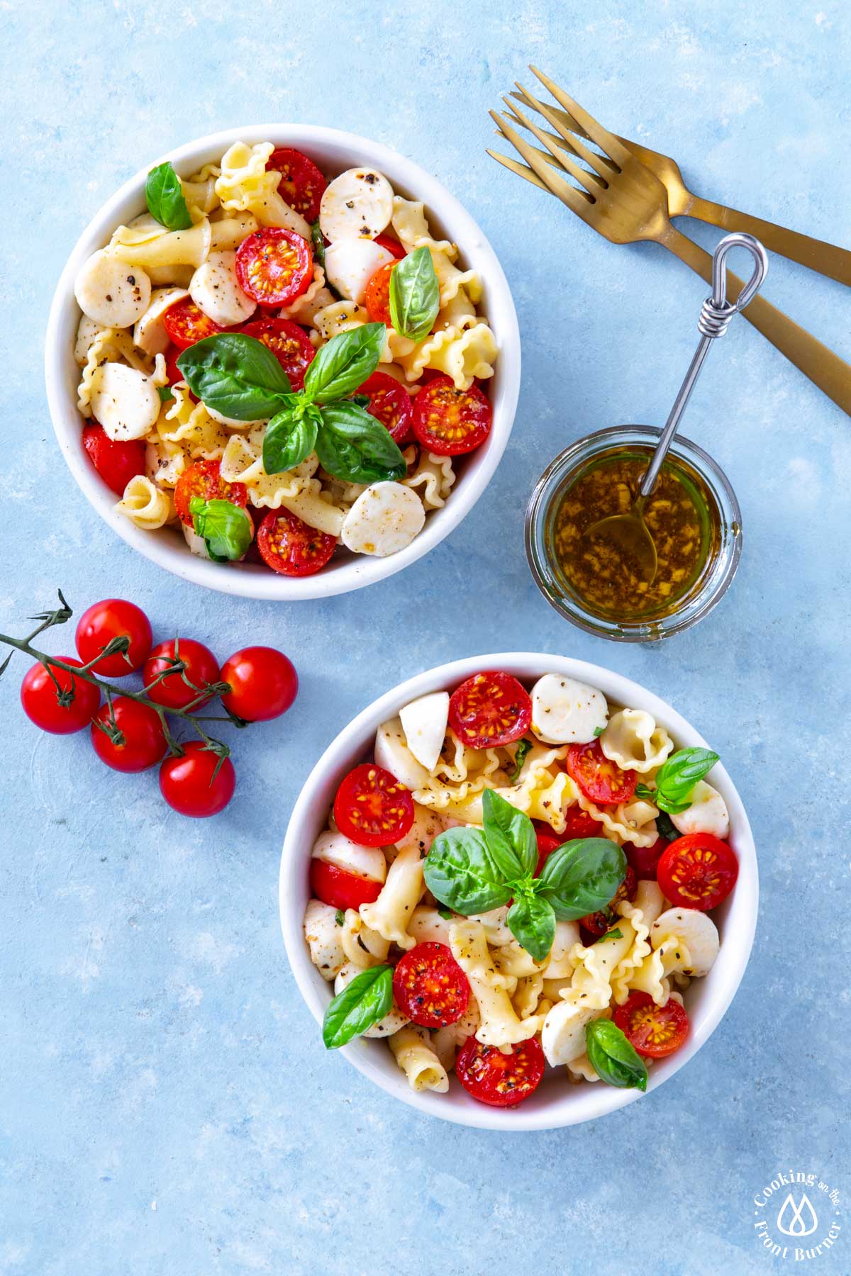 two white bowls with caprese pasta salad with vinaigrette in a bowl on side
