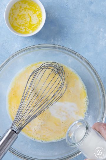 milk pouring into whisked eggs in a clear bowl